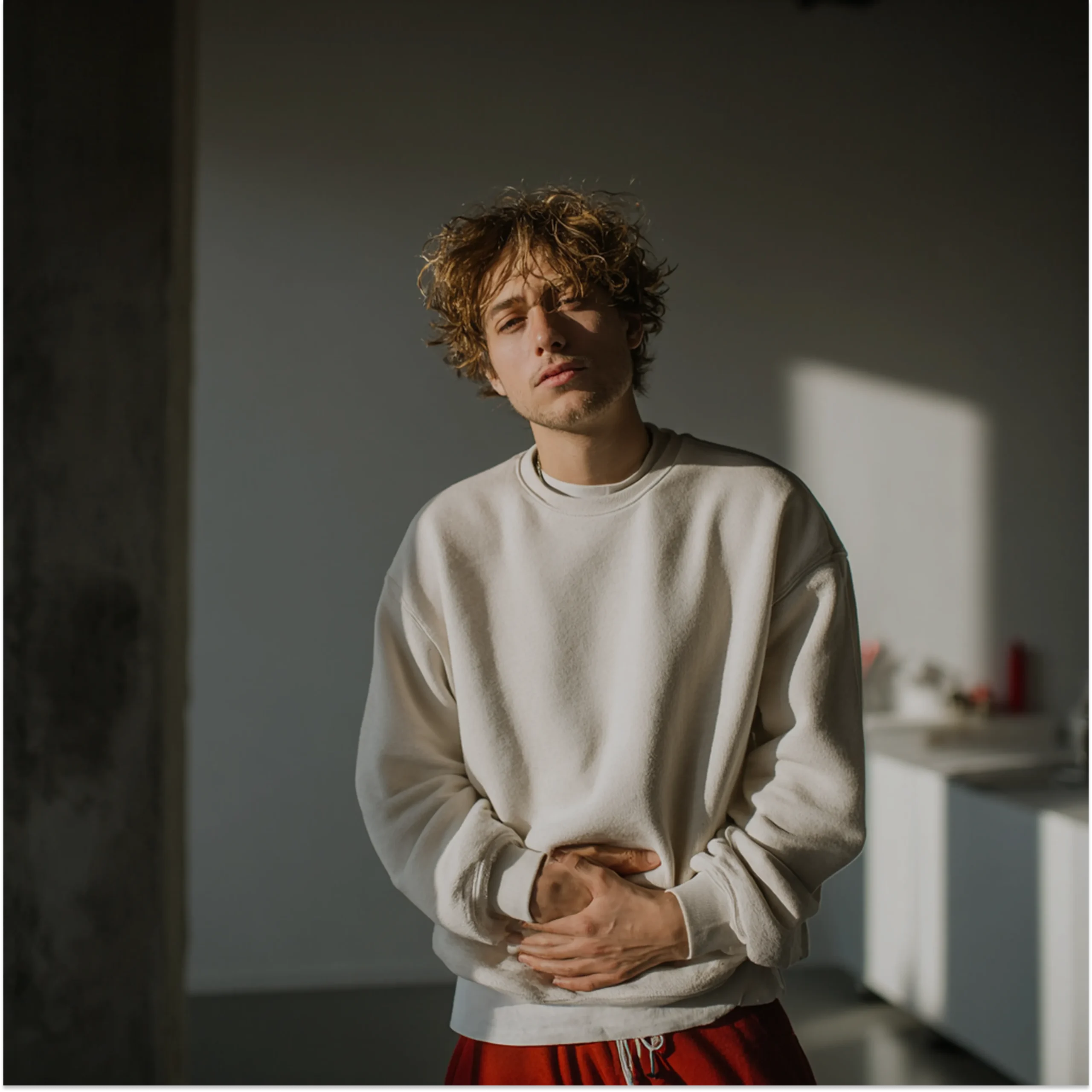 młody mężczyzna o blond włosach z grymasem na twarzy trzyma się za brzuch